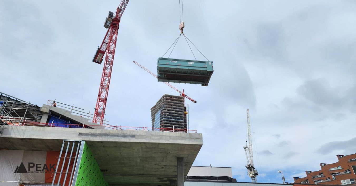 Crane lifting dumpster at construction site, illustrating access constraints like overhead clearance, tight spaces, and delivery limitations