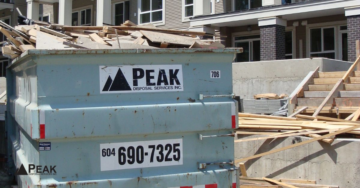 Large teal Peak Disposal bin filled with construction debris at a residential building site in BC.