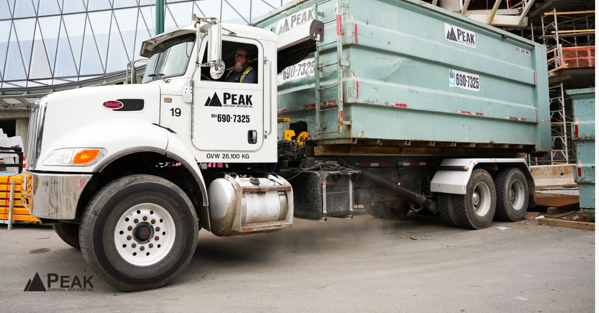 Peak Disposal roll-off truck with driver delivering a large green bin at a Surrey construction site.