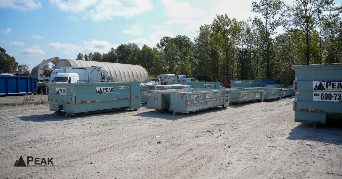 Row of teal Peak Disposal bins lined up at a sunny outdoor storage yard surrounded by trees in BC.