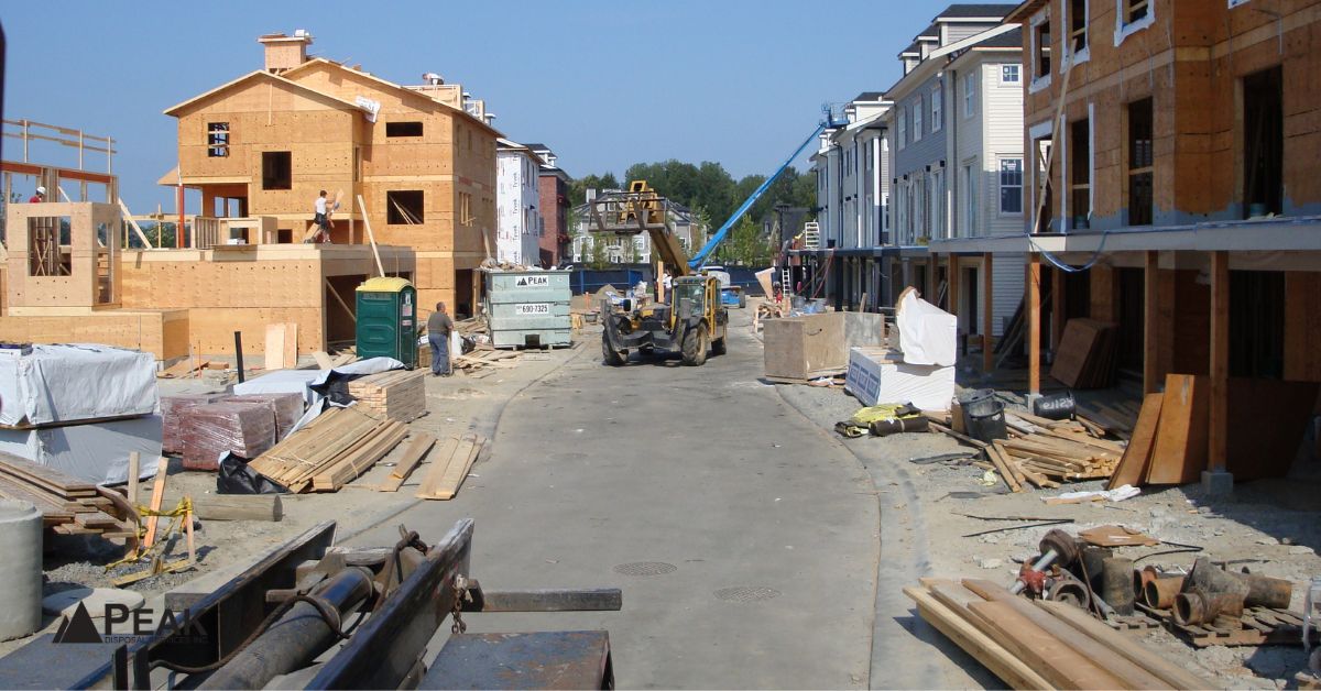 Busy residential construction site in BC with multiple buildings, scattered materials, and a Peak Disposal bin.