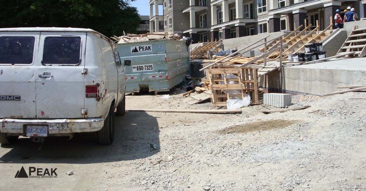 White van parked beside a teal Peak Disposal bin at a busy BC construction site.
