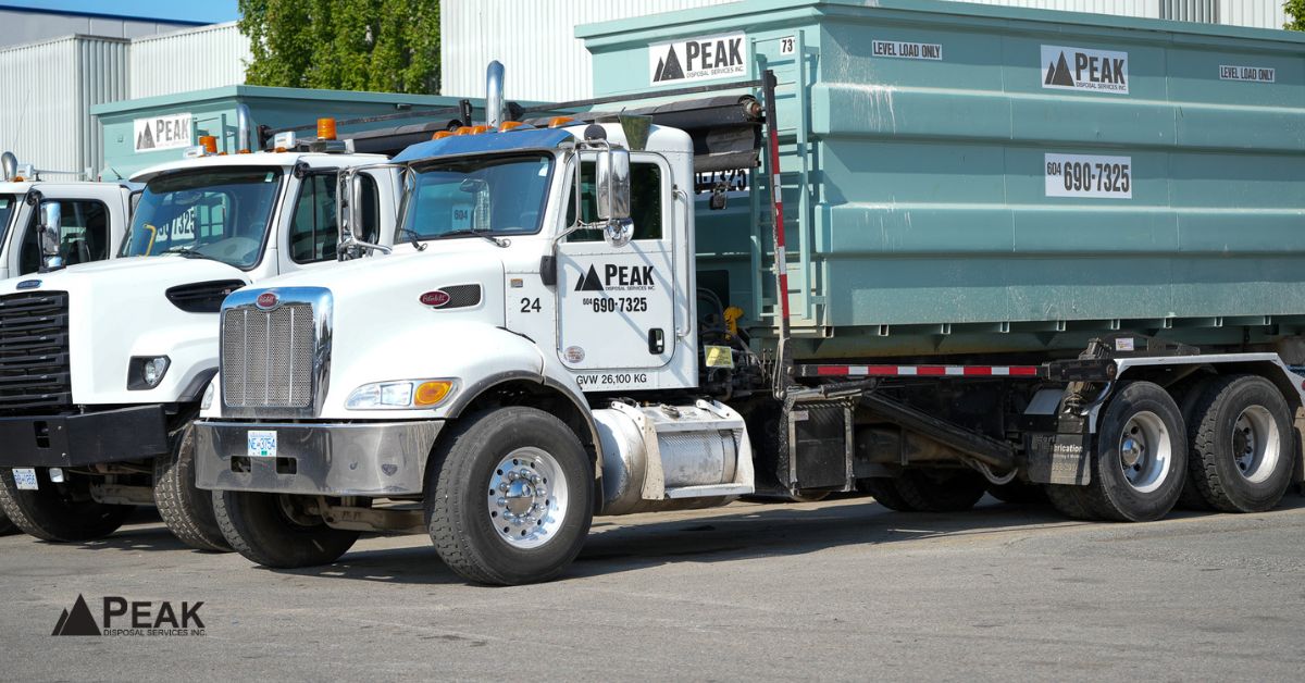 White Peak Disposal roll-off truck with teal drywall bin parked at a BC disposal yard.