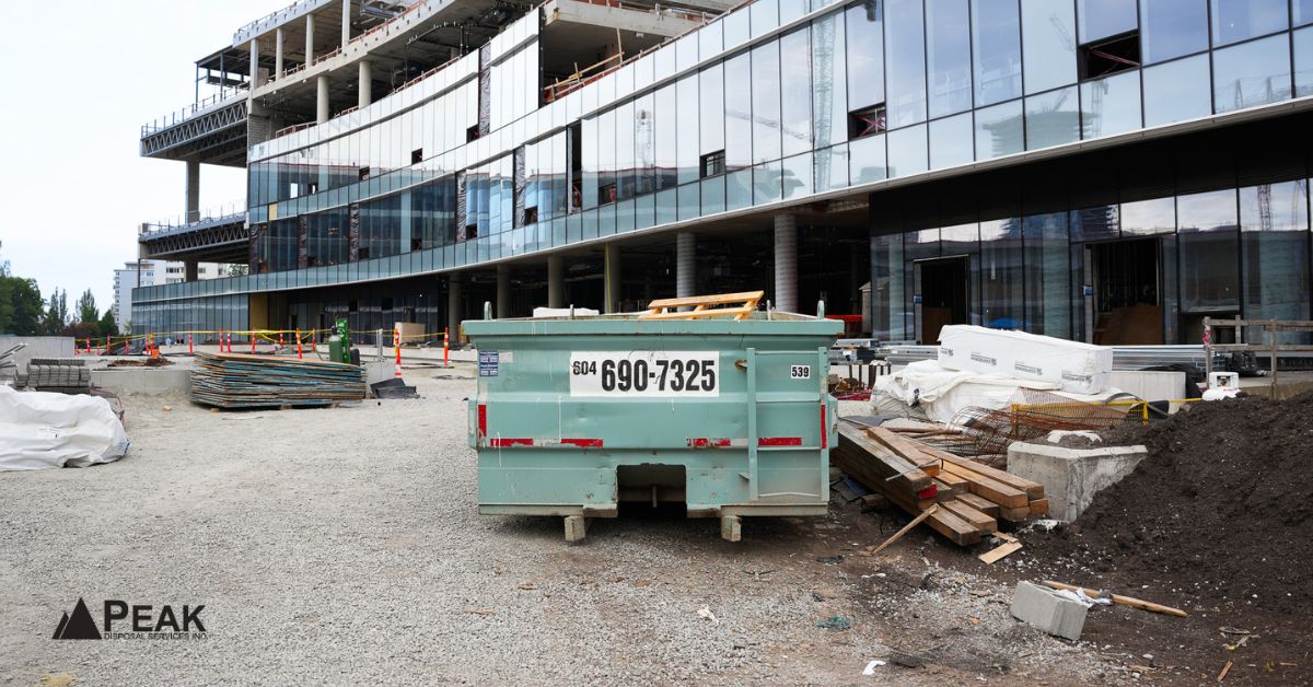 Construction site in Vancouver with a teal dumpster in the foreground and a large glass building under construction in the background