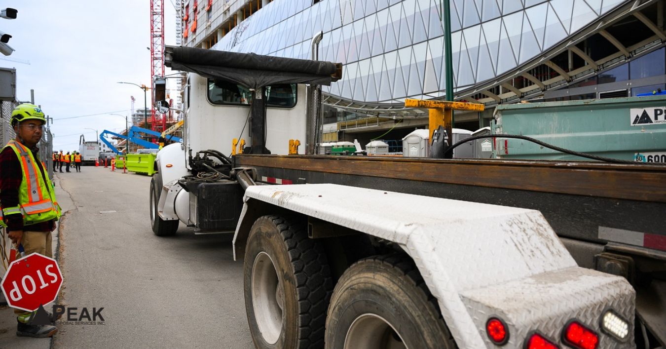 Construction site worker guiding bin truck placement on street, ensuring safe positioning, traffic flow, and access compliance in Coquitlam
