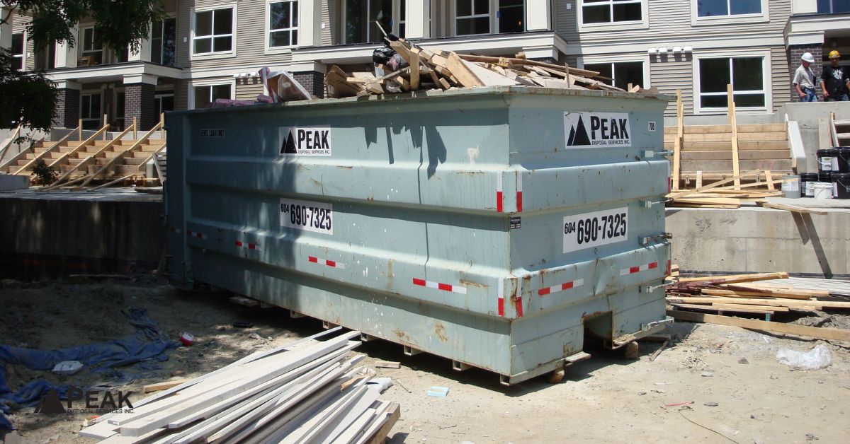 Large blue construction dumpster filled with mixed debris at a BC building site, highlighting regulated drywall disposal.