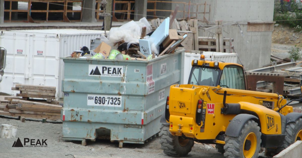 Construction dumpster overflowing beside telehandler illustrates mixed waste contamination, inconsistent disposal practices, and diversion reporting challenges onsite.
