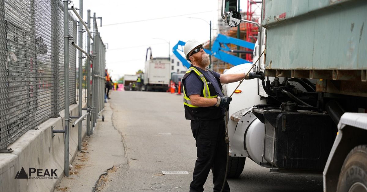Worker in safety vest guiding a large white roll-off truck positioning a dumpster on a residential driveway