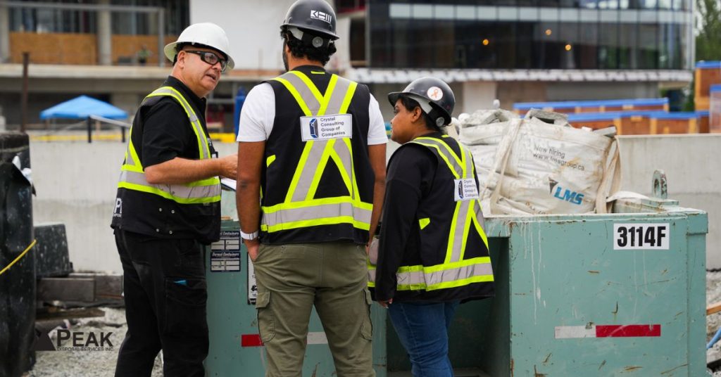 Construction team reviewing waste management documentation beside disposal bins to support LEED reporting, diversion tracking, and compliance requirements.