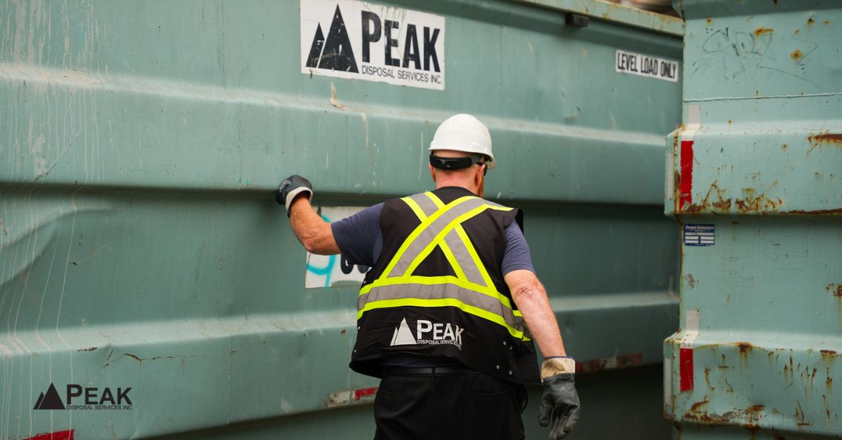 Construction worker managing disposal container to support waste diversion reporting, material tracking, landfill reduction, and LEED documentation compliance.