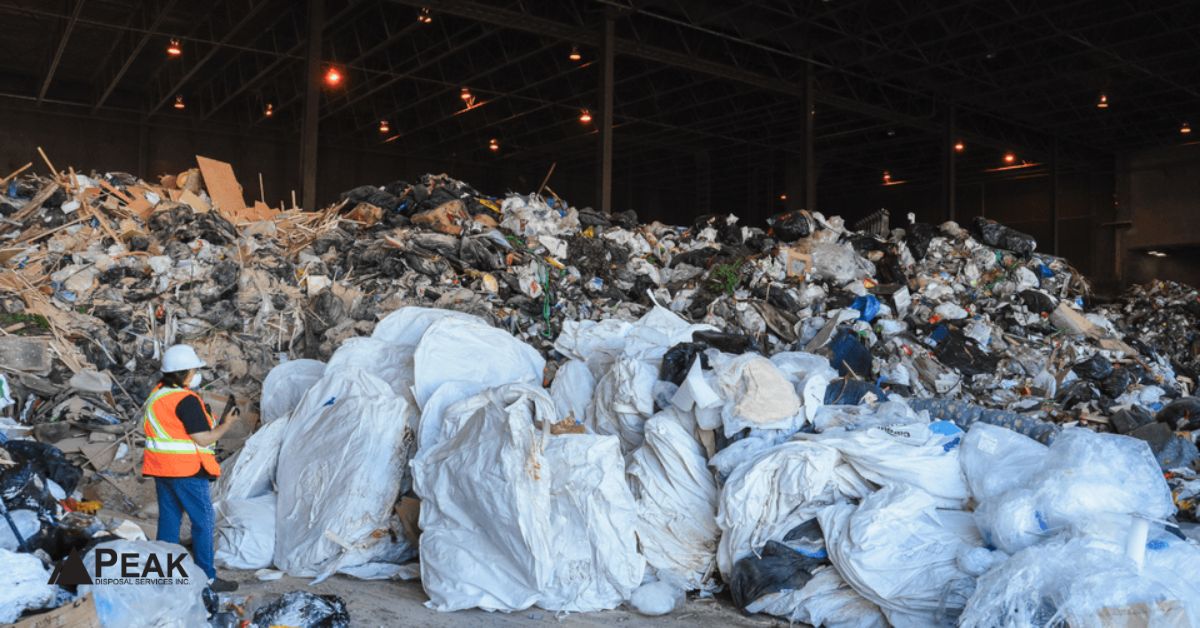Worker inspecting commercial construction waste inside Metro Vancouver transfer station processing recyclable and mixed material streams.