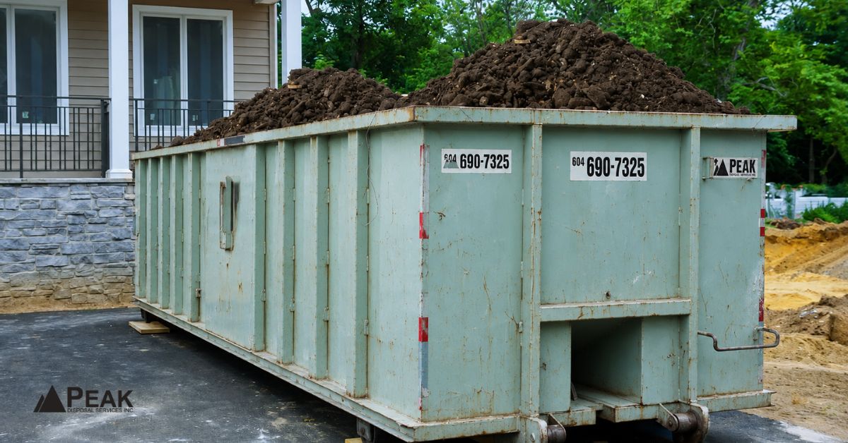 Green clean fill bin loaded with soil at a residential construction site beside a house and driveway.