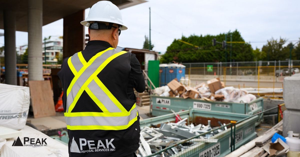 Construction worker at active job site with multiple dumpsters, showing preferred waste management solution for ongoing construction projects.