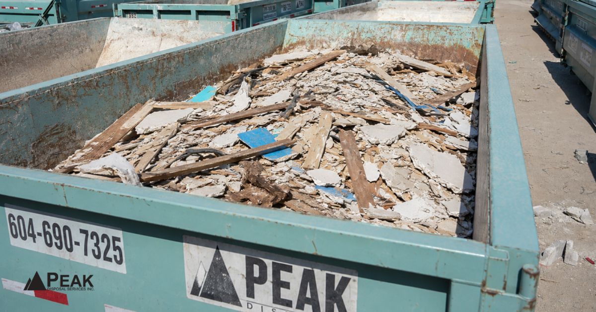 PEAK DISPOSAL dumpster filled with mixed construction waste including broken drywall, wood scraps, and contaminated debris