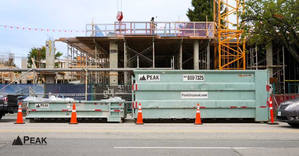 PEAK Disposal dumpsters positioned beside active construction site with safety cones and partially built structure nearby.