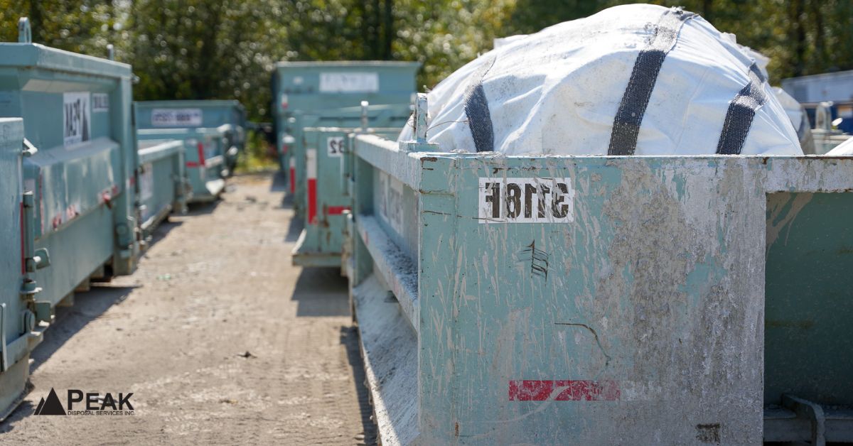 Row of green Peak Disposal dumpsters lined up at the yard, one covered with a large white bag – simplifying waste managemen