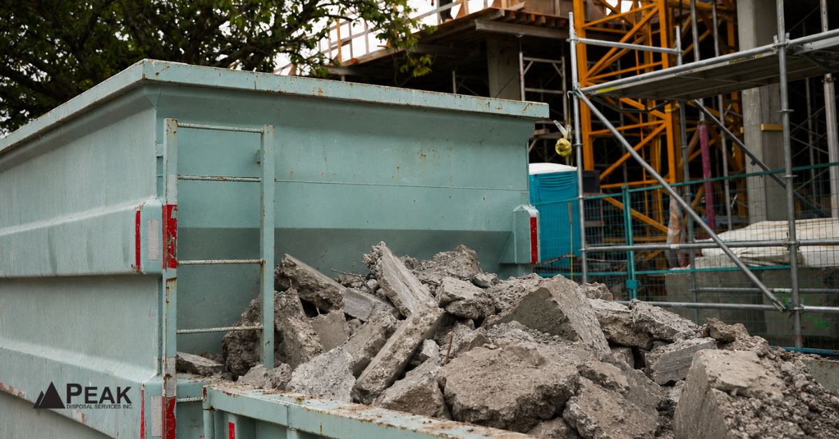 Partially filled concrete dumpster at active construction site, showing dense rubble despite significant unused container space.